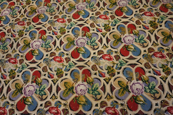 Multi-colored low pile rug displays purple and red flowers against a cream gothic-style geometric trellis.