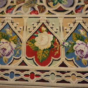 Close-up of a low-pile rug with repeating Gothic arch patterns featuring cream roses on red and blue grounds.