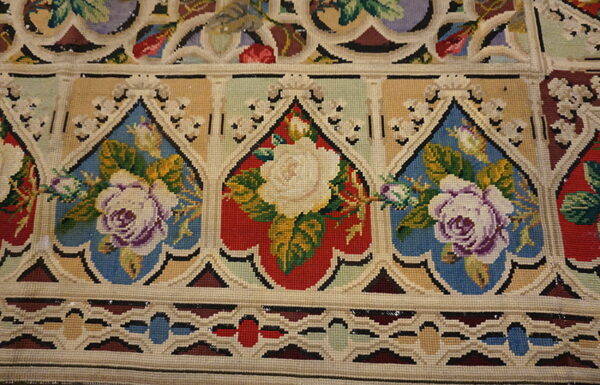Close-up of a low-pile rug with repeating gothic arch patterns featuring cream roses on red and blue grounds.
