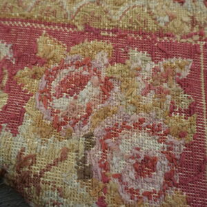 Macro view of a rug showing intricate floral patterns in tan, reddish-pink, and beige looped fibers.