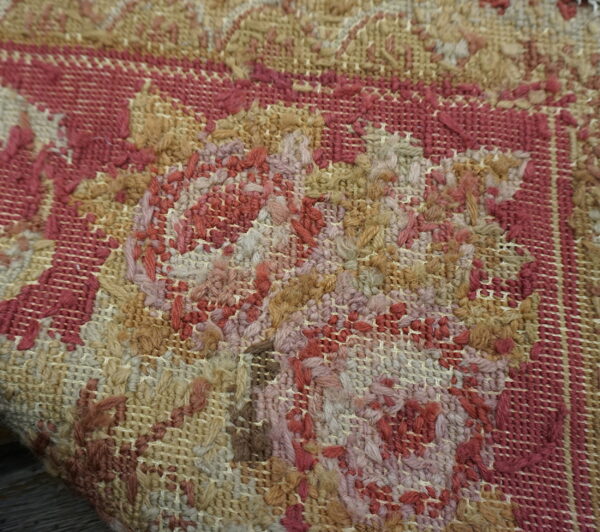 Macro view of a rug showing intricate floral patterns in tan, reddish-pink, and beige looped fibers.