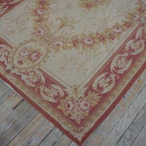 Low-pile rug in beige, dusty rose, and gold floral patterns rests on distressed gray wooden plank flooring.