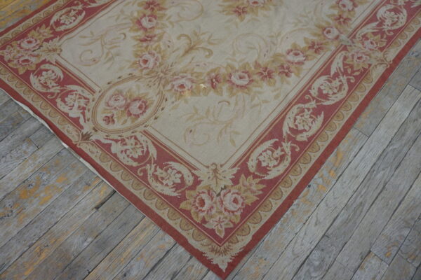 Low-pile rug in beige, dusty rose, and gold floral patterns rests on distressed gray wooden plank flooring.
