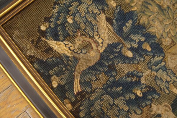 Close-up of a low-pile framed textile featuring a tan bird among dense blue and olive foliage.