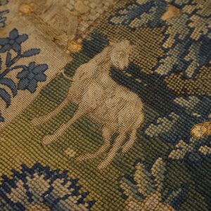 Worn flatweave rug detail featuring a tan animal motif surrounded by blue and olive green patterns.