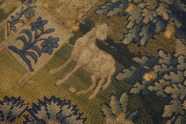 Worn flatweave rug detail featuring a tan animal motif surrounded by blue and olive green patterns.
