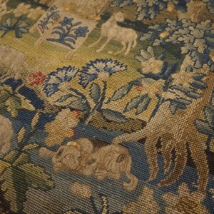 Muted blue, green, and beige framed tapestry textile with a detailed animal and floral scene design.
