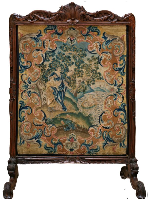 Needlepoint tapestry depicting a central scene framed by blue and tan scrolls, mounted in a carved wood screen.