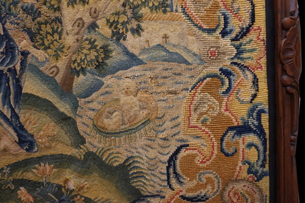 Low-pile woven rug close-up in blue and tan, showing woven damage beside a carved dark wood frame.