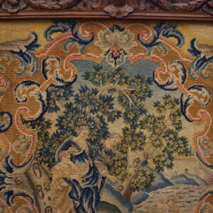 Framed tapestry depicting a pastoral scene with figures, surrounded by an ornate golden yellow and blue border.