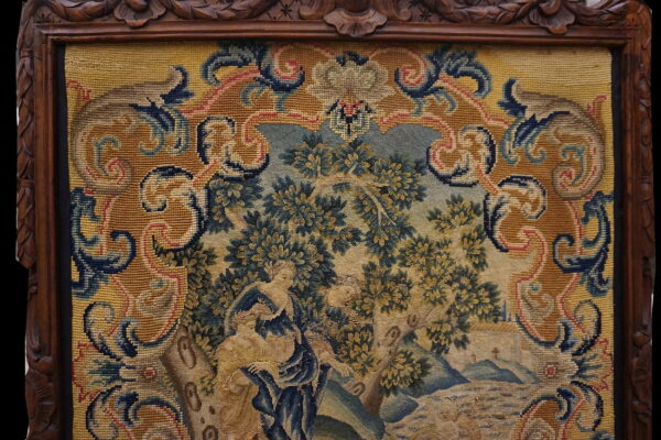 Framed tapestry depicting a pastoral scene with figures, surrounded by an ornate golden yellow and blue border.