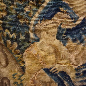 Close view of a damaged, tan flatweave rug with abstract dark blue and green woven patterns.