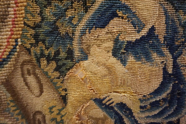 Close view of a damaged, tan flatweave rug with abstract dark blue and green woven patterns.