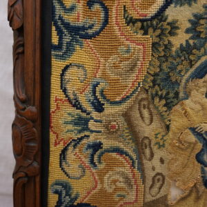 Close-up of a framed, gold and blue figurative tapestry with visible wear and a carved wood border.