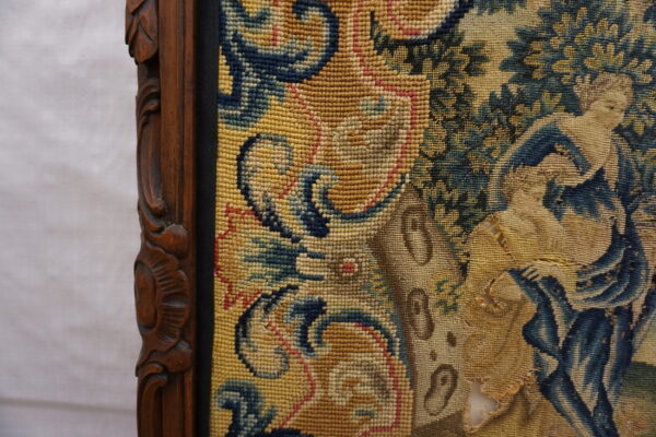 Close-up of a framed, gold and blue figurative tapestry with visible wear and a carved wood border.