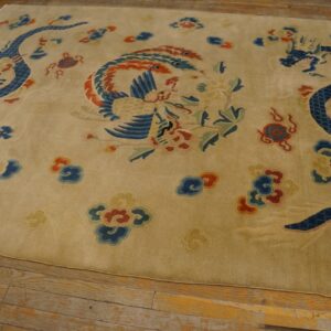 Tan rug with intricate blue dragon and multicolored phoenix pattern rests on distressed wooden flooring.