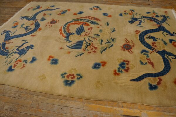 Tan rug with intricate blue dragon and multicolored phoenix pattern rests on distressed wooden flooring.