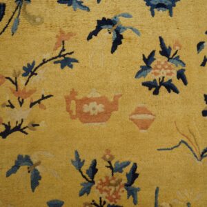 Golden yellow high-pile rug with navy, light blue, and pink stylized flower and teapot patterns on wood flooring.