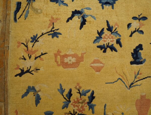 Golden yellow high-pile rug with navy, light blue, and pink stylized flower and teapot patterns on wood flooring.