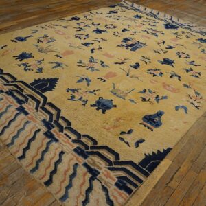 Gold rug featuring scattered blue and coral patterns and a dark blue geometric border on wood plank flooring.