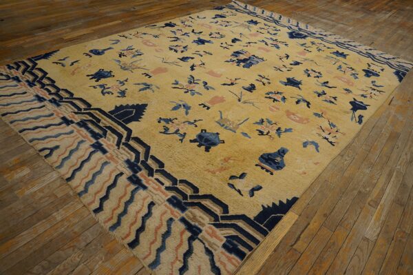 Gold rug featuring scattered blue and coral patterns and a dark blue geometric border on wood plank flooring.