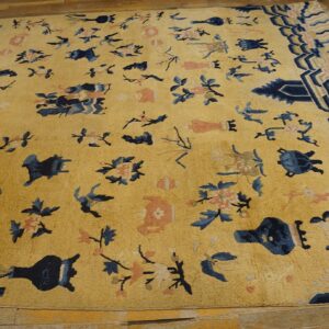 Yellow-gold rug with scattered blue and coral motifs and geometric borders displayed on hardwood flooring.
