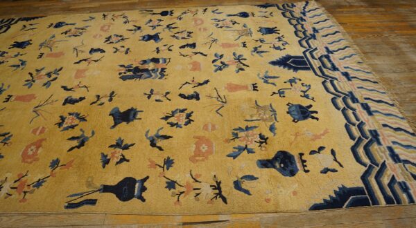 Yellow-gold rug with scattered blue and coral motifs and geometric borders displayed on hardwood flooring.