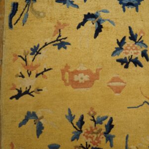 Golden yellow rug with blue and coral floral and teapot motifs rests on rustic wood plank flooring.