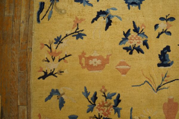 Golden yellow rug with blue and coral floral and teapot motifs rests on rustic wood plank flooring.