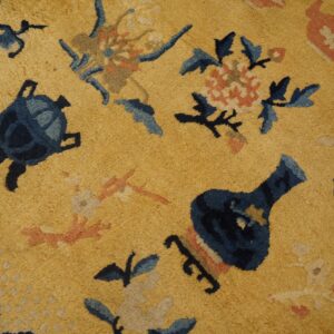 Golden yellow rug texture detail featuring traditional motifs like dark blue turtles, vases, and pink flowers.