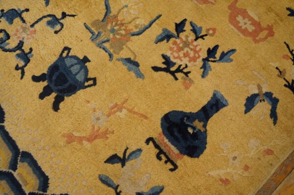 Golden yellow rug texture detail featuring traditional motifs like dark blue turtles, vases, and pink flowers.