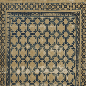 Navy blue scrolling lattice pattern on a distressed tan rug, framed by Greek key and medallion borders.