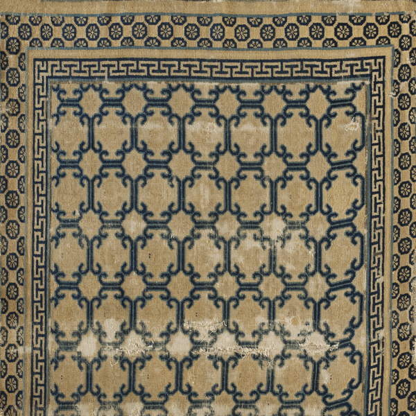 Navy blue scrolling lattice pattern on a distressed tan rug, framed by greek key and medallion borders.