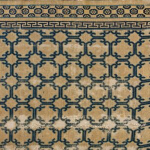 Tan rug with a distressed low pile features a repeating dark blue geometric lattice and Greek key border.