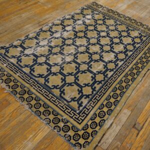 Low pile blue and tan geometric patterned rug with distressed areas on worn wood plank flooring.