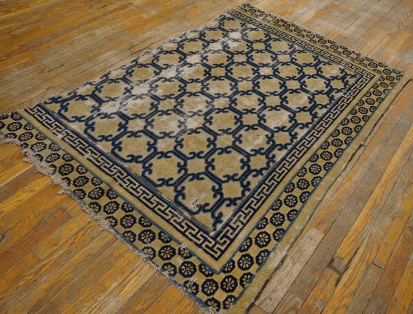 Low pile blue and tan geometric patterned rug with distressed areas on worn wood plank flooring.