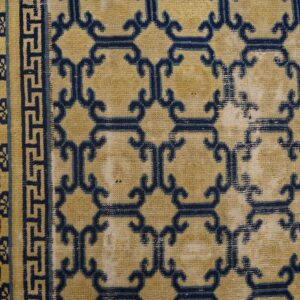 Worn tan rug features dark blue geometric trellis and patterned borders on wood flooring.