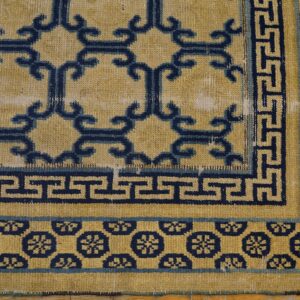 Distressed yellow rug with navy blue scroll and geometric key borders on natural wood flooring.