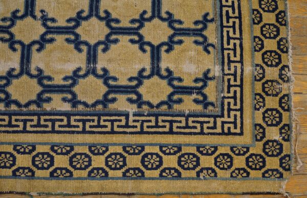 Distressed yellow rug with navy blue scroll and geometric key borders on natural wood flooring.