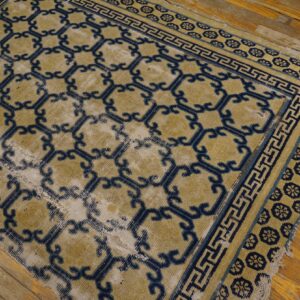 Gold and indigo geometric rug, featuring low pile and extensive wear, lies on rustic wooden flooring.