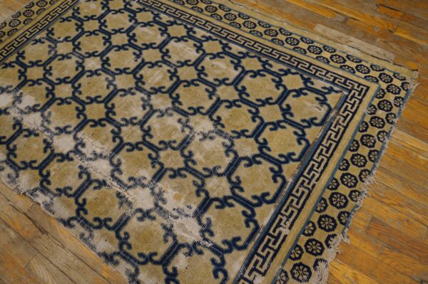 Gold and indigo geometric rug, featuring low pile and extensive wear, lies on rustic wooden flooring.