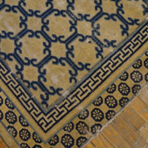 Golden yellow rug with navy scroll and key borders rests on distressed hardwood flooring.