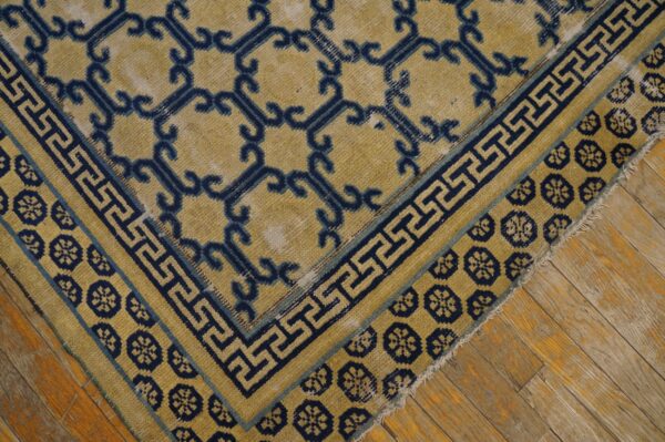 Golden yellow rug with navy scroll and key borders rests on distressed hardwood flooring.