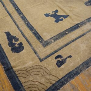 A distressed tan and blue low-pile rug with abstract patterns rests on worn wooden planks.