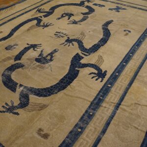 Worn, khaki and navy rug with large dragon motifs and a striped geometric border over wood flooring.