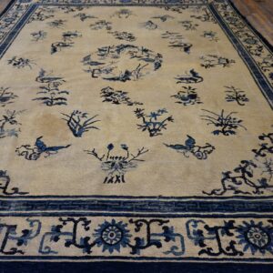 Light beige rug with scattered dark blue floral and bird patterns bordered by complex geometric designs on wood planks.