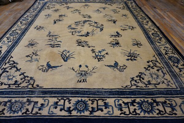 Light beige rug with scattered dark blue floral and bird patterns bordered by complex geometric designs on wood planks.