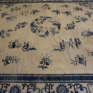 Cream low-pile rug featuring scattered dark blue floral motifs, a central medallion, and an elaborate border.