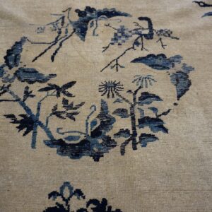 Textured beige rug with a circular motif of dark and light blue stylized plants and flowers.