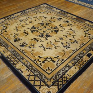 Ornate square rug in cream, gold, and navy blue with geometric borders on wood floor.